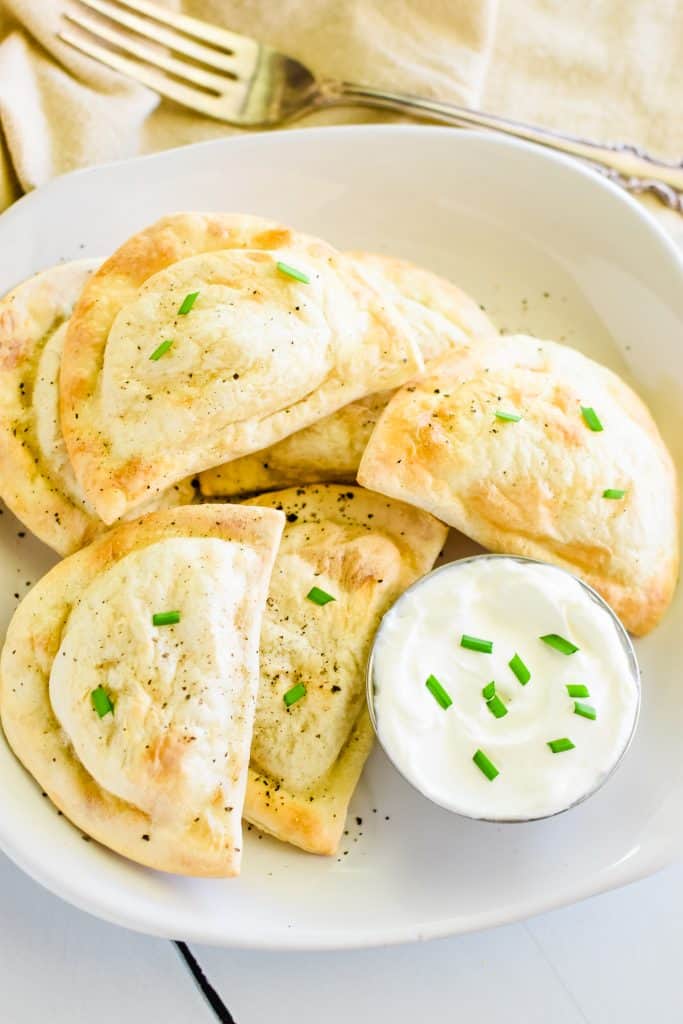 overhead of air fryer pierogies on a white plate topped with chives and black pepper and some sour cream on the side