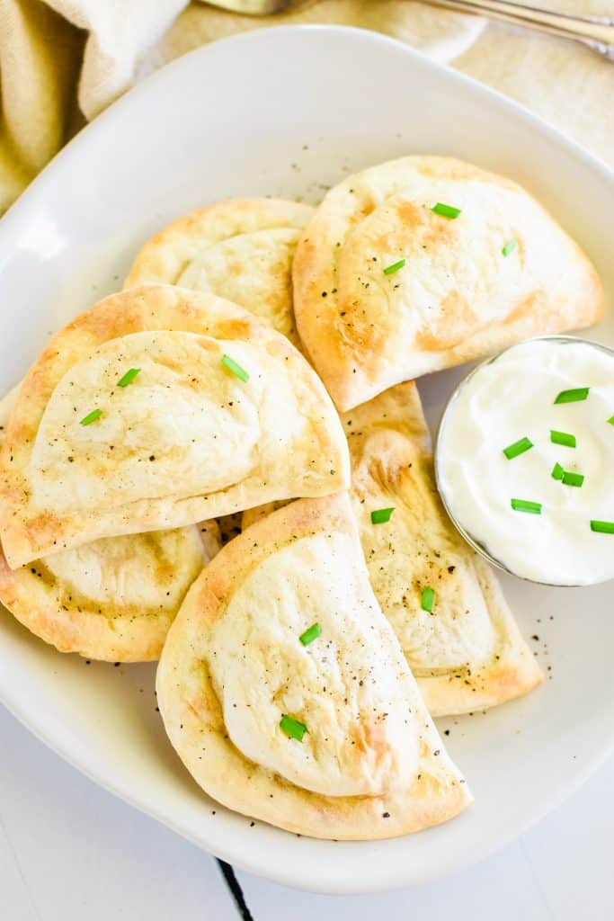 overhead of pierogies on white plate with part of the side of sour cream cut out
