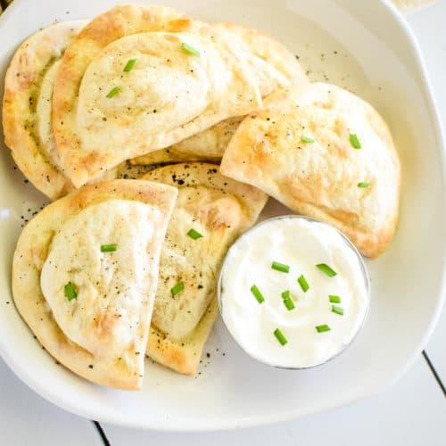 overhead of pierogies on a white plate with black pepper and chives and with side of sour cream