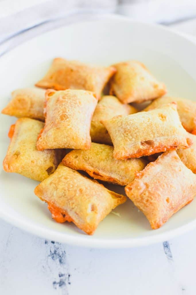 front view of pizza rolls on white plate with some cheese oozing out.