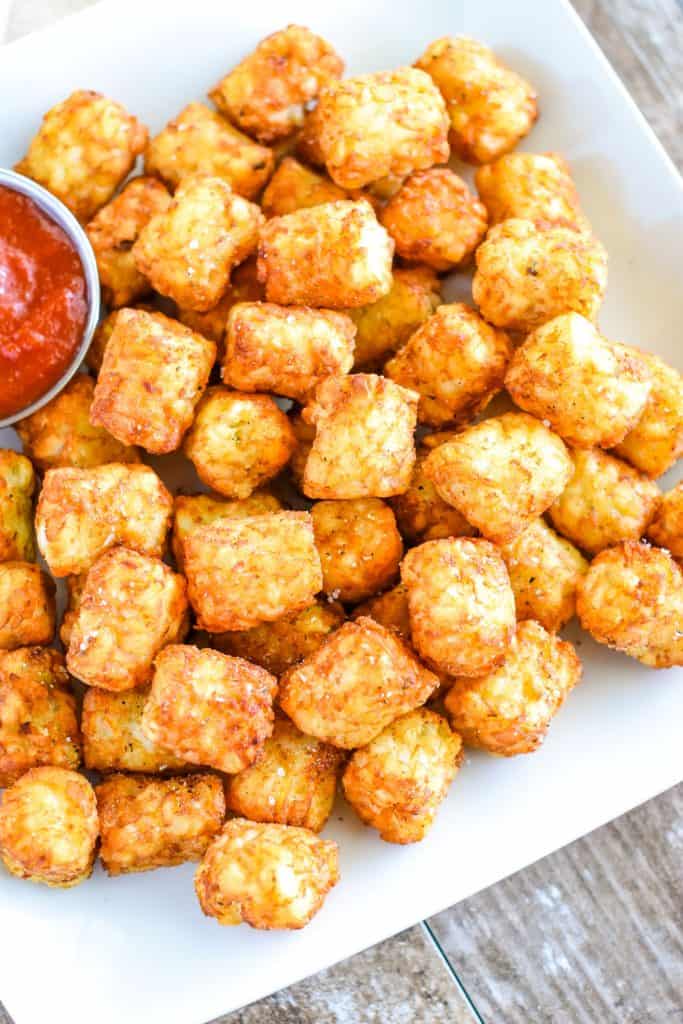 overhead of air fryer tater tots on white plate with side of ketchup on left side partly cut off