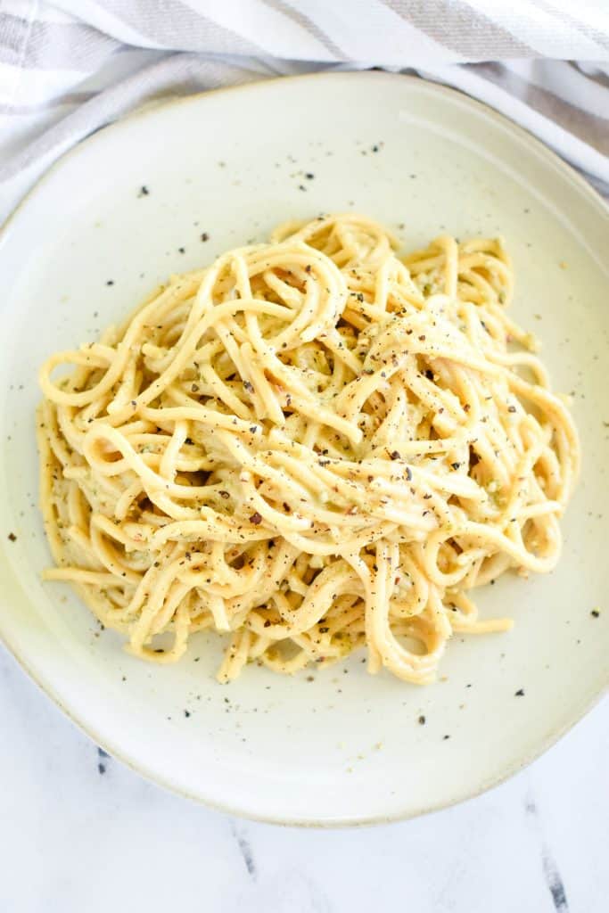 overhead of vegan cacio e pepe on a white plate garnished with more black pepper