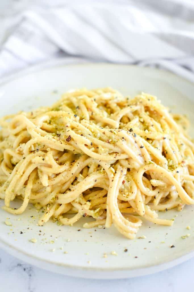 close-up front view of pasta on white serving dish garnished with pepper and pumpkin seed Parmesan