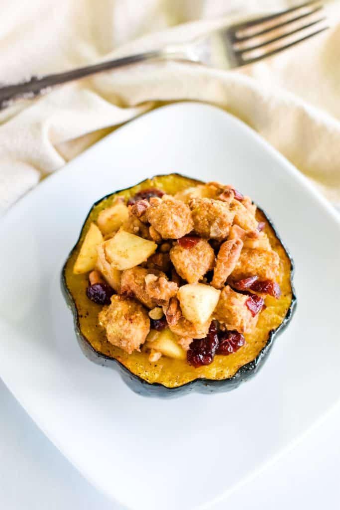 Above serving of vegan stuffed acorn pumpkin on a white plate with a fork behind it