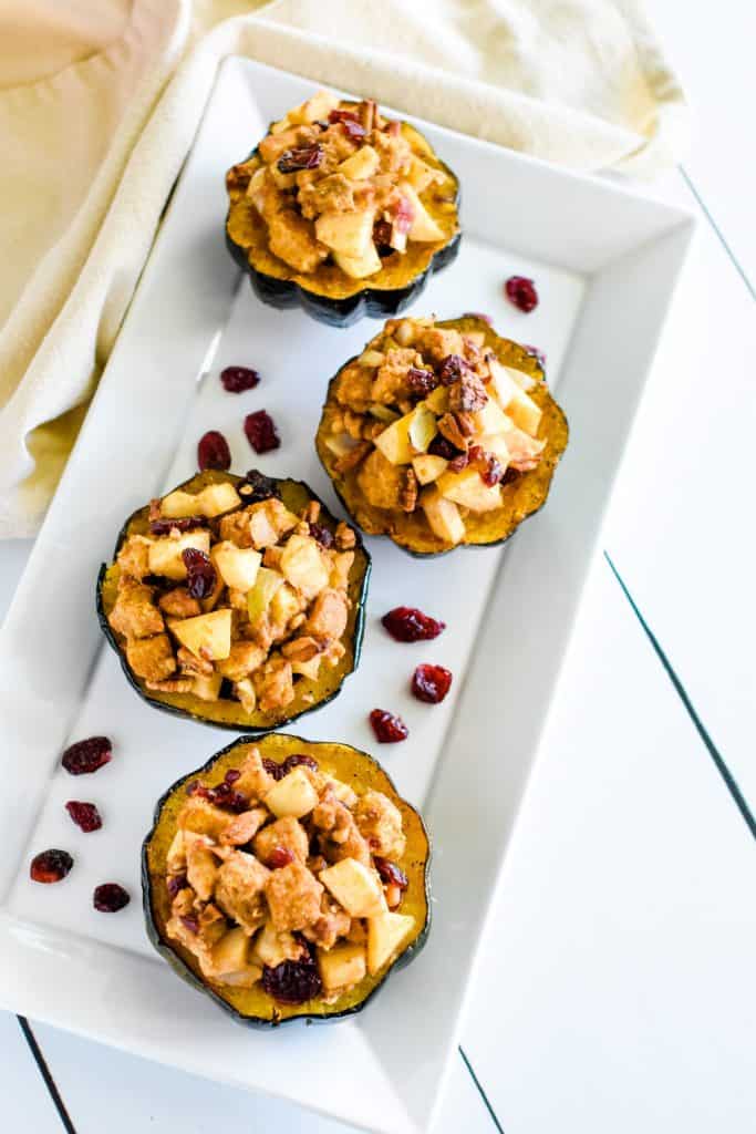 overhead of 4 servings of stuffed acorn squash on white platter with dried cranberries around