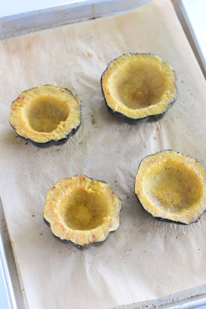4 acorn squash halves face up on parchment-lined baking sheet after roasting