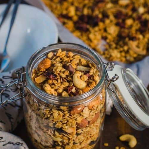 granola in a mason jar with the lid open and some on the table and some blurred out behind it