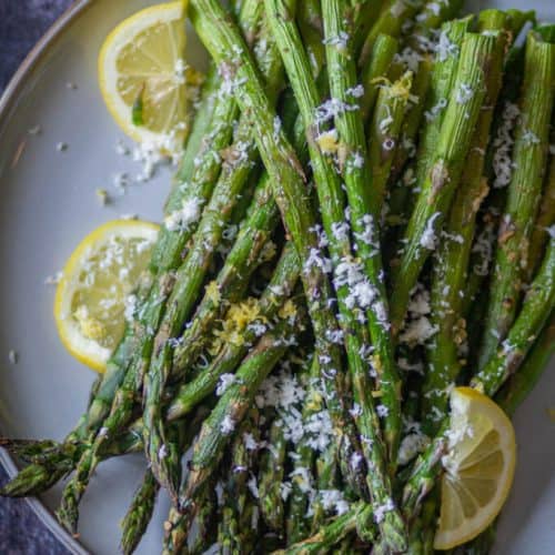 overhead of asparagus garnished with Parmesan and sliced lemons on the side