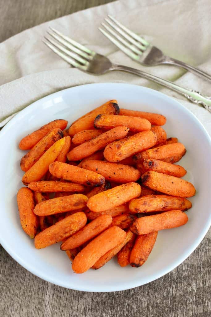 overhead of carrots on a white plate with two forks behind it