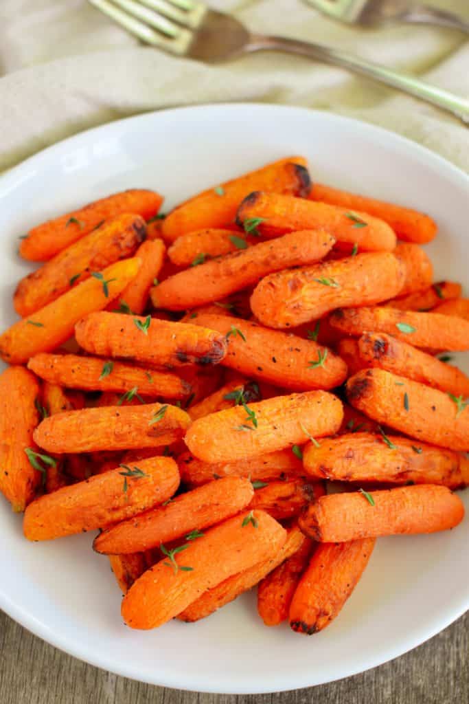 close-up overhead of air fryer carrots on a white plate garnished with fresh thyme leaves