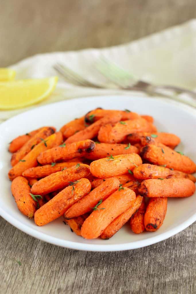 slight overhead of carrots on a white plate with lemon wedges and forks blurred out behind it