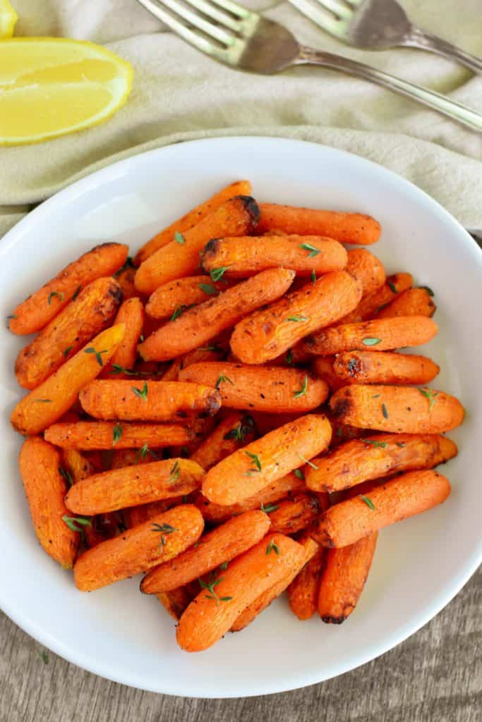 overhead of carrots on a white plate with lemon wedges and forks behind it