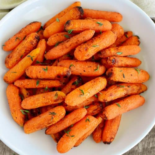 close-up overhead of carrots on a white plate garnished with fresh thyme