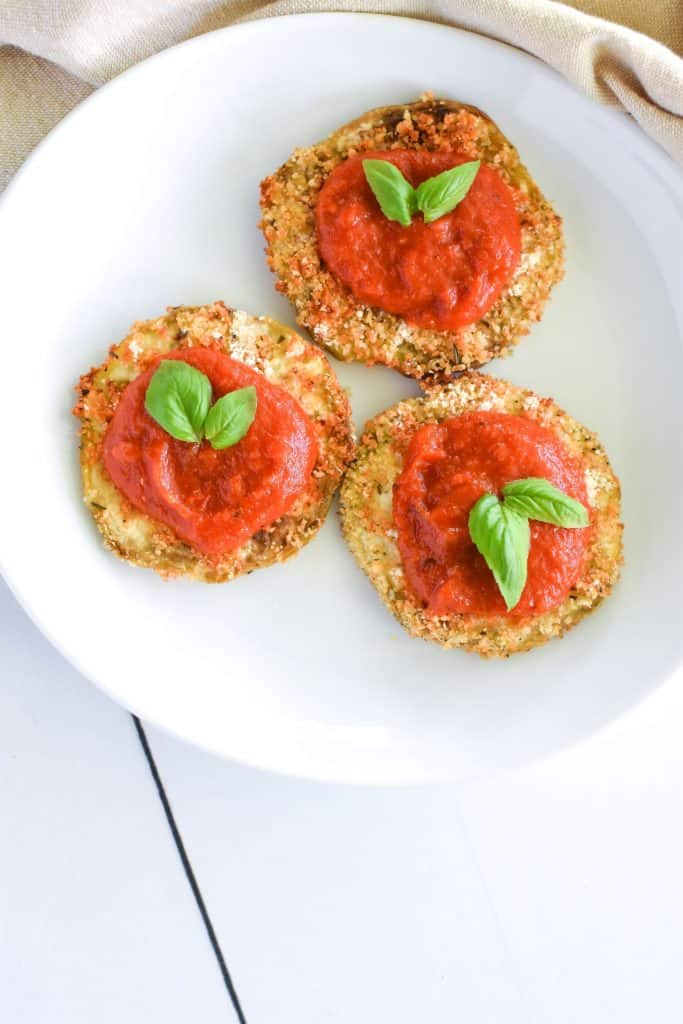 overhead of eggplant slices topped with tomato sauce and garnished with basil on a white plate