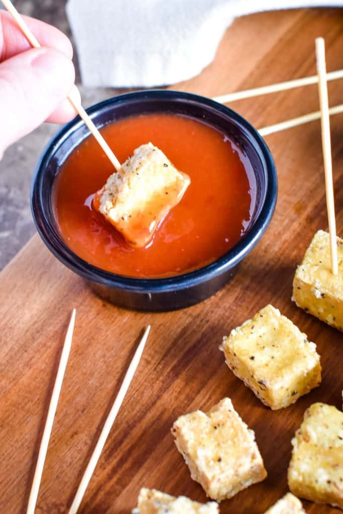 Dipping a piece of tofu into sweet chili sauce with a serving toothpick.