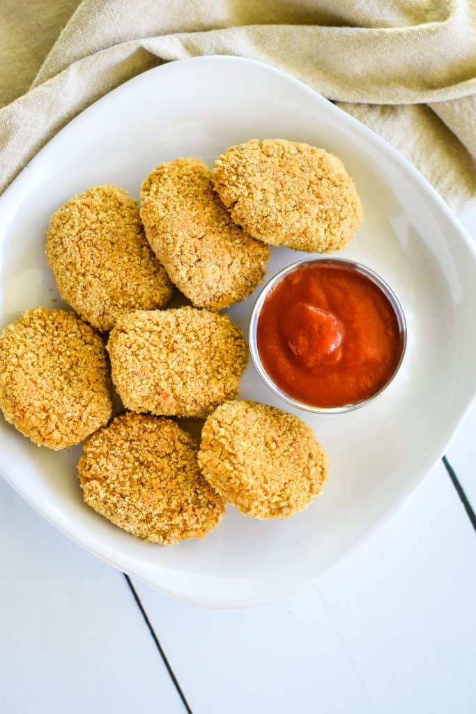 overhead of nuggets on a white plate with small cup of ketchup to the right of them on the plate