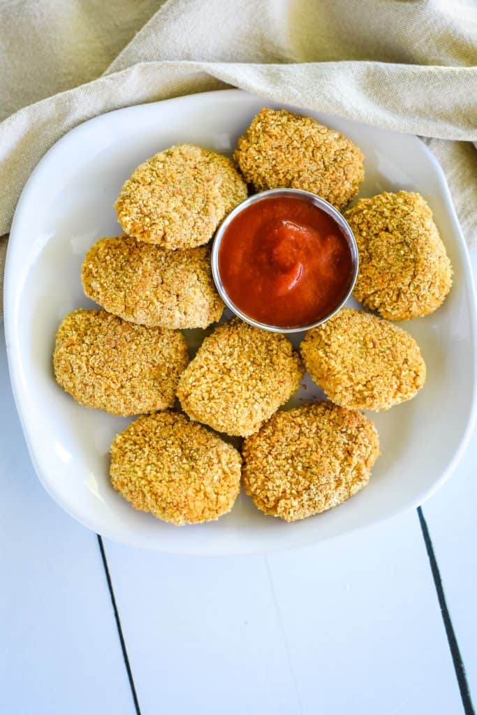 farther away overhead of chickpea nuggets on a white plate with small cup of ketchup