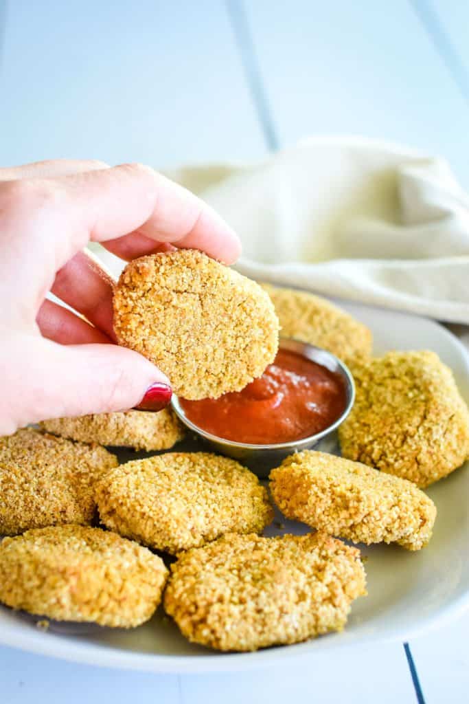dipping a nugget into ketchup on a white plate with more nuggets