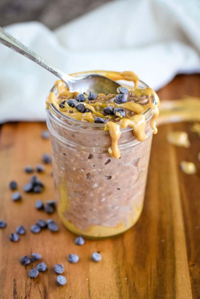 front view of oats in a mason jar with spoon in it and extra peanut butter and chips on top