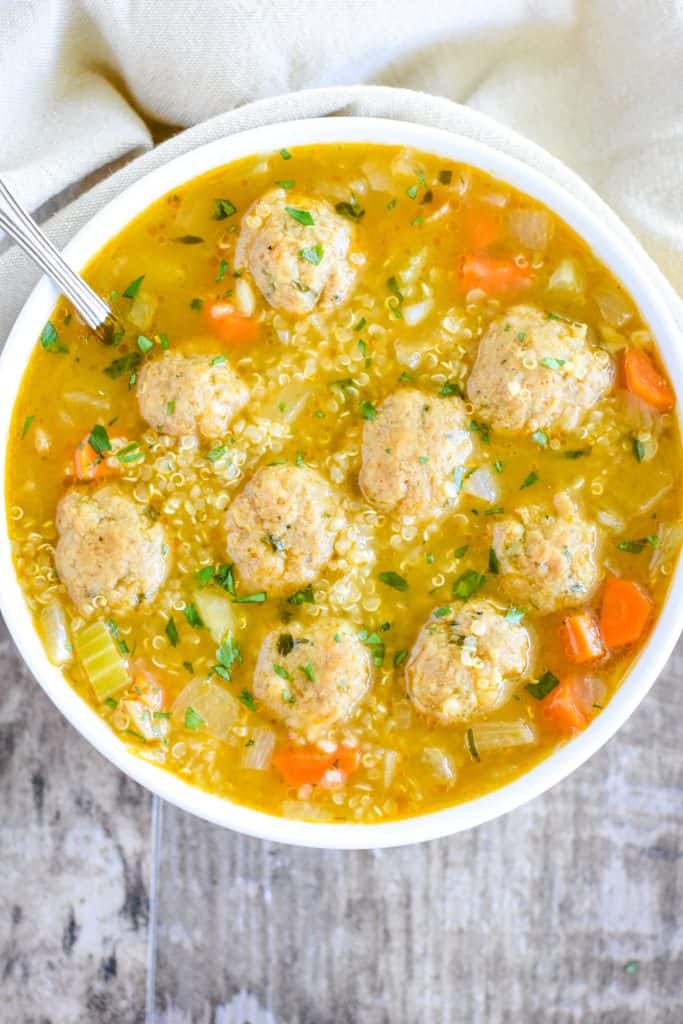 overhead shot of quinoa soup with mini vegan meatballs in white bowl with spoon in it