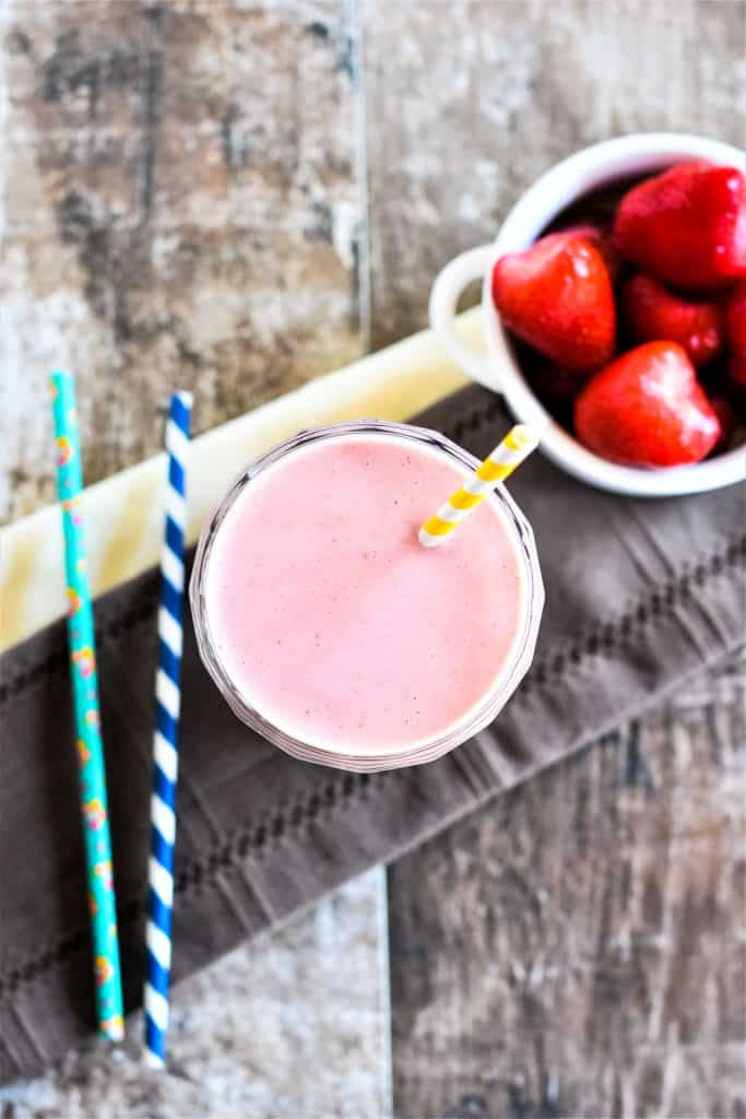overhead of strawberry-banana peanut butter smoothie with straw in it and strawberries and straws off to the sides