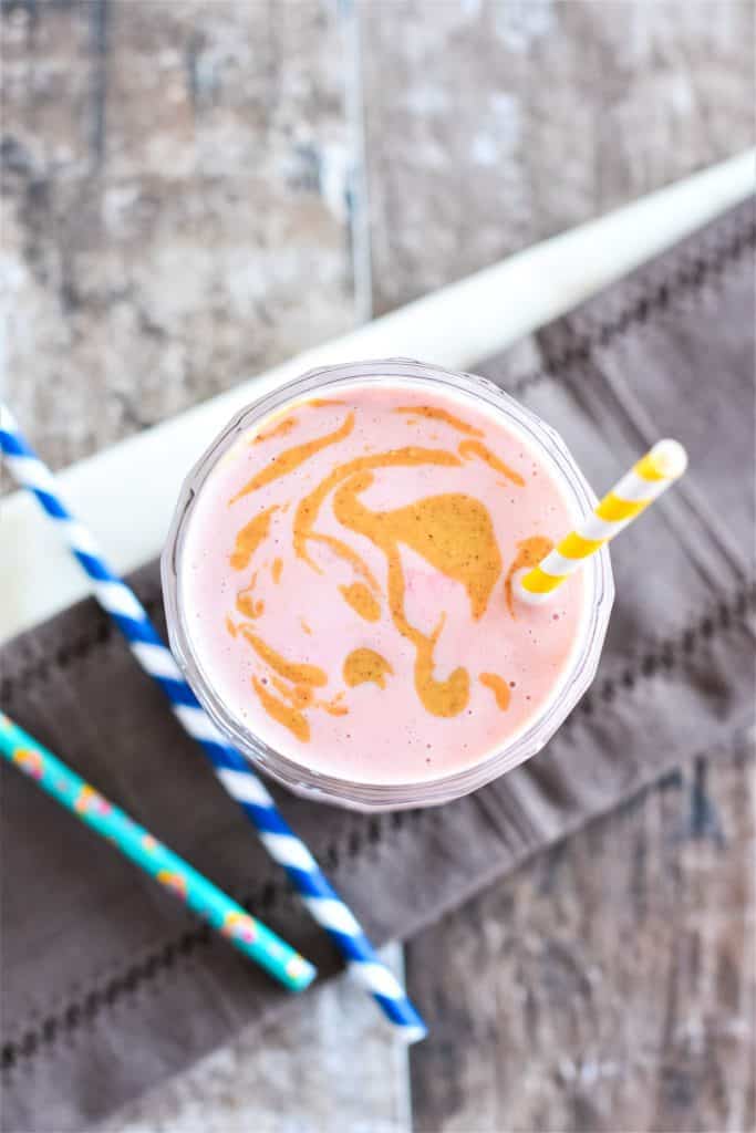overhead of smoothie in a glass with a straw and peanut butter swirled on top