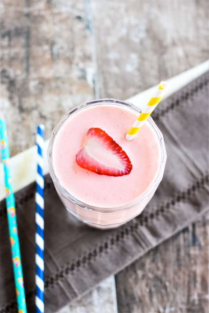 overhead of smoothie in a glass with a cut strawberry in the middle and a straw in it