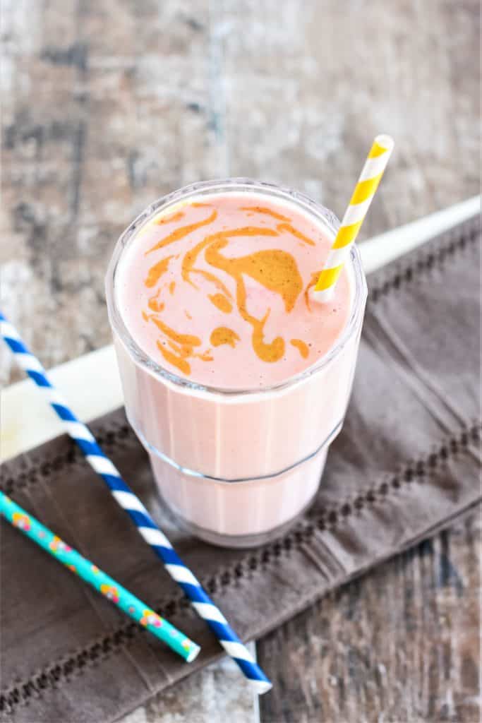 slight overhead of peanut butter smoothie with some peanut butter swirled on top and a straw in it