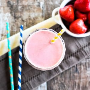 overhead of smoothie in a glass with straw in it and straws and strawberries off to the sides