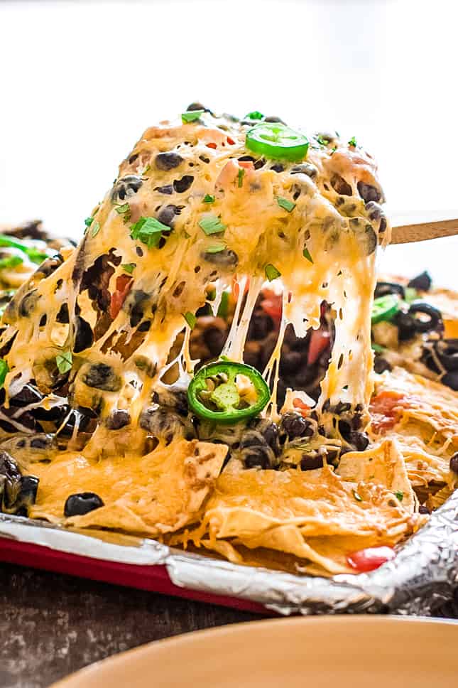 scooping up nachos from the sheet pan with cheese pulling