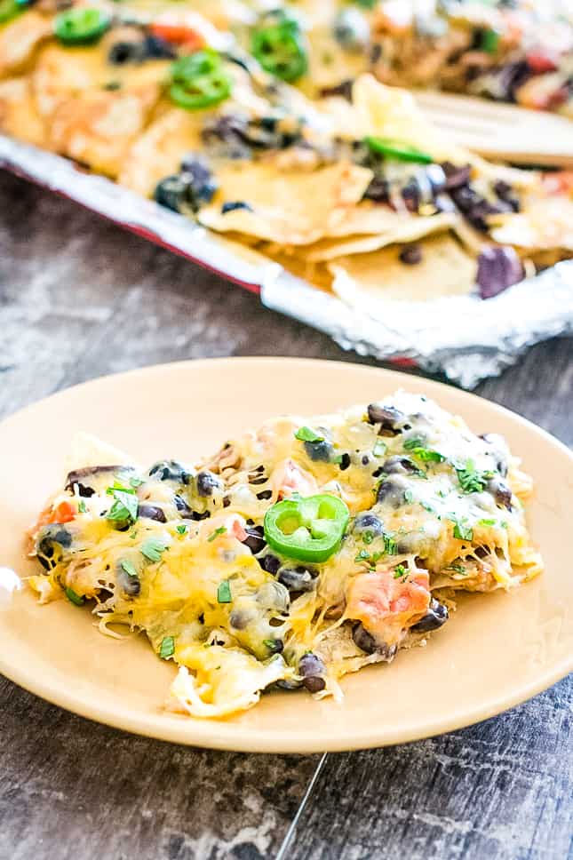 serving of nachos on a plate with the rest on the sheet pan behind it