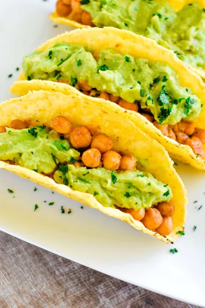 3 chickpea tacos on a white plate with guacamole and cilantro garnish.