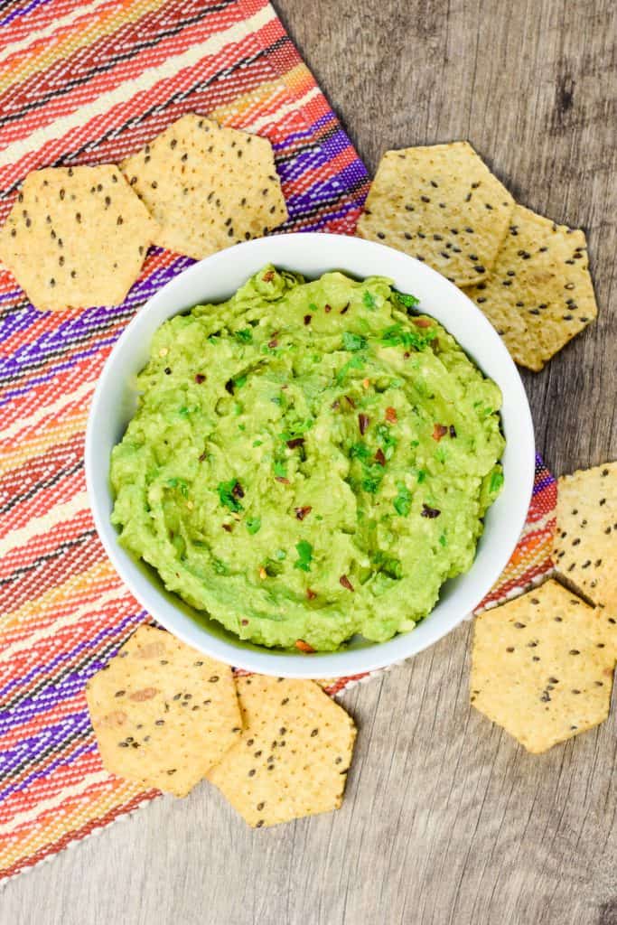 overhead of guacamole in white bowl with chips around.