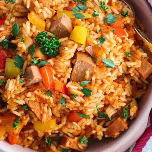overhead of rice with sausage and peppers in a dish with spoon in it.