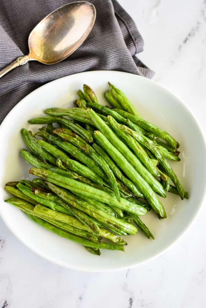 overhead of air fryer green beans on white plate with spoon back left.