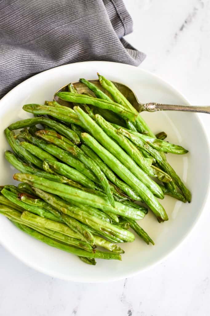 overhead of green beans on a white plate with spoon scooping some.