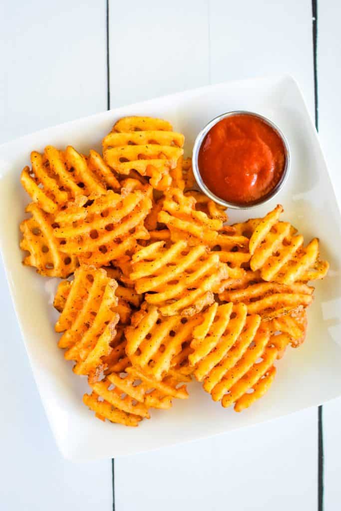 overhead of waffle fries on a white plate with ketchup.