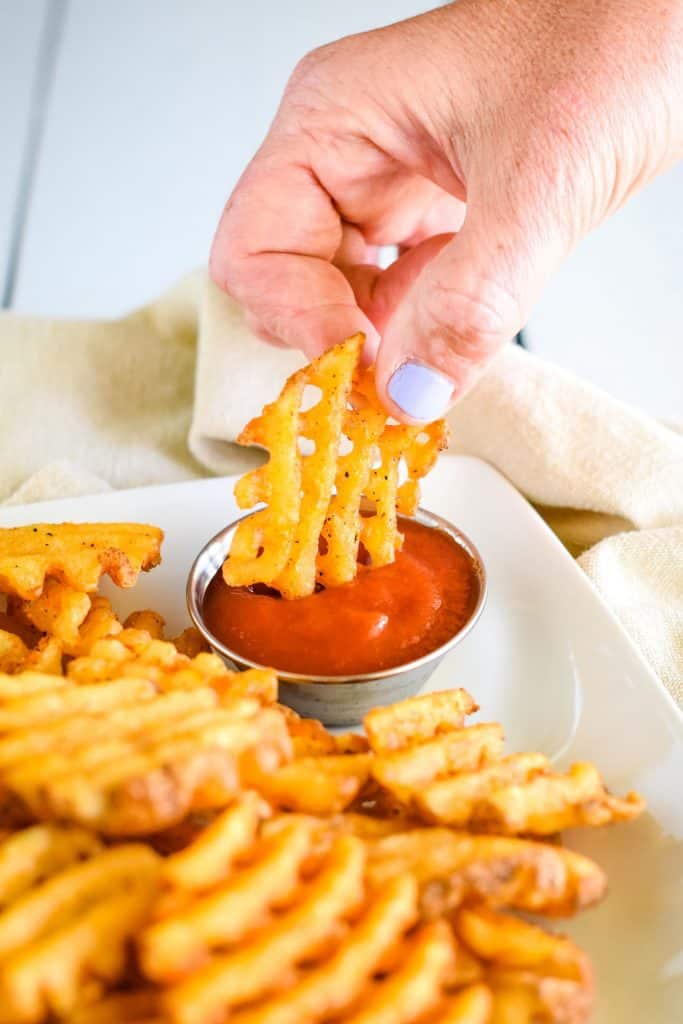 hand dipping a fry into ketchup.