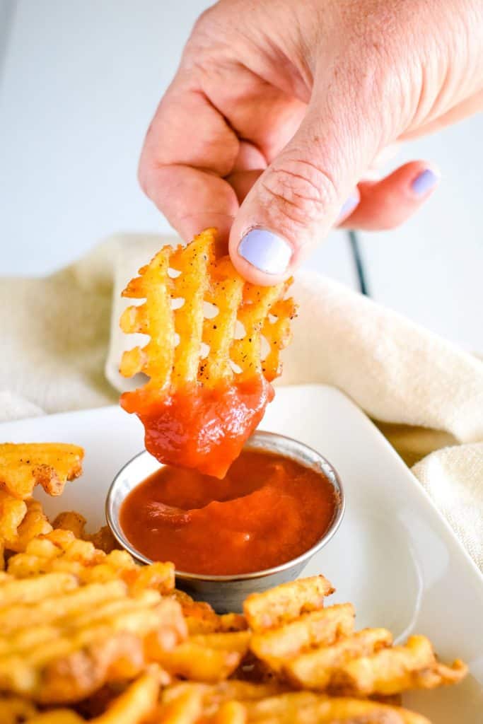 holding waffle fry after dipping into ketchup.
