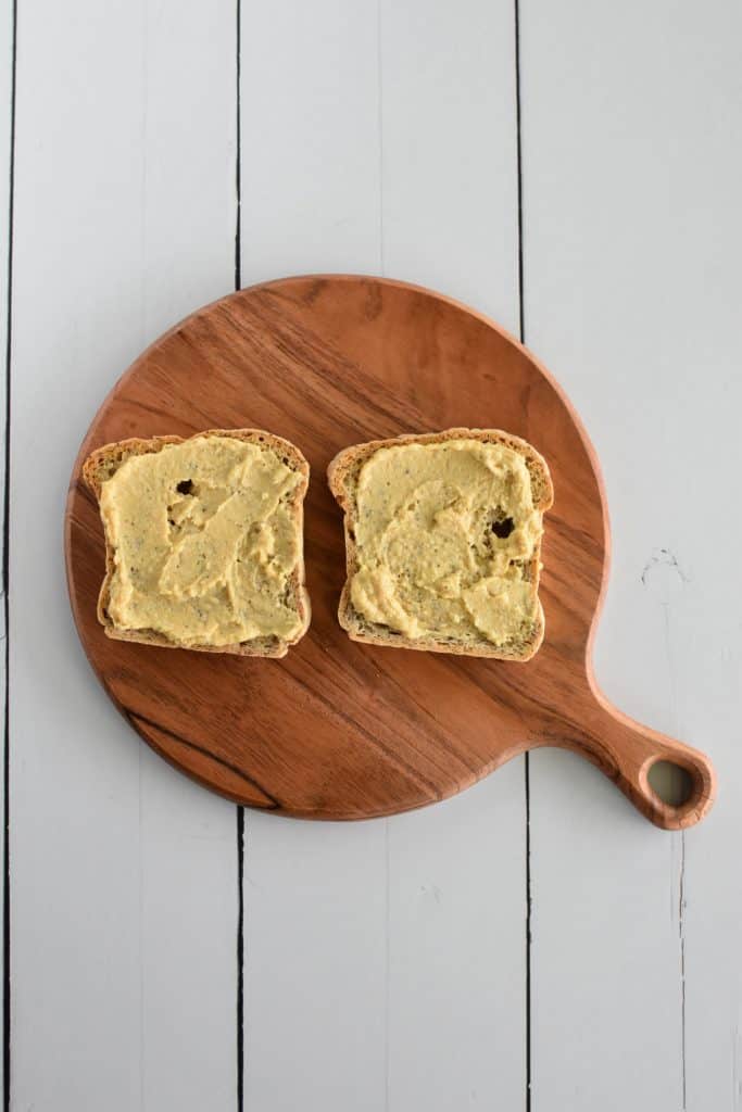 two slices of toast with hummus on them on a wooden board.