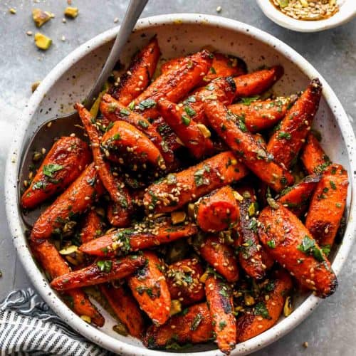 overhead of roasted carrots in a white bowl with a spoon in it.