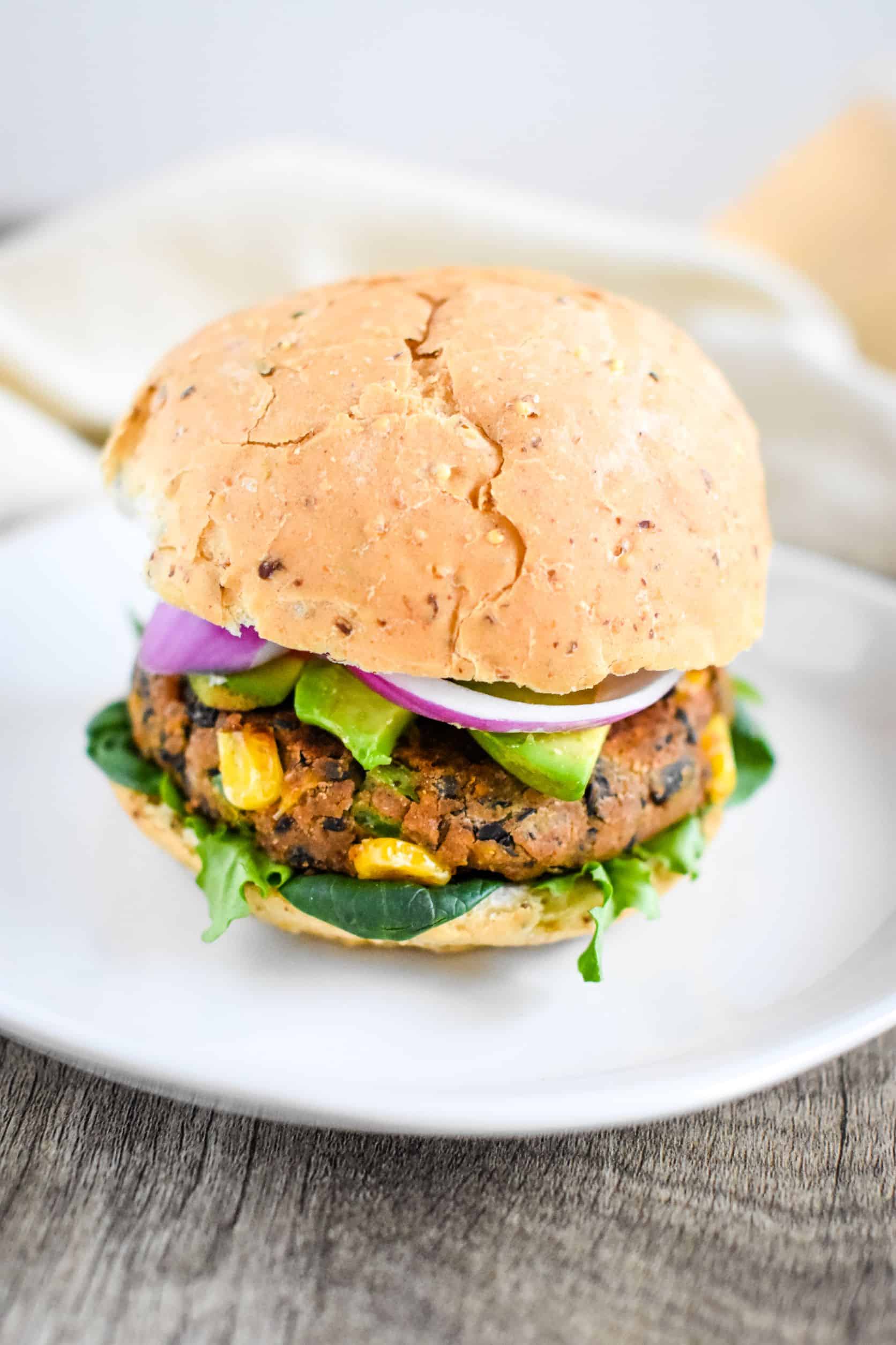 veggie burger with avocado and red onion on a white plate.
