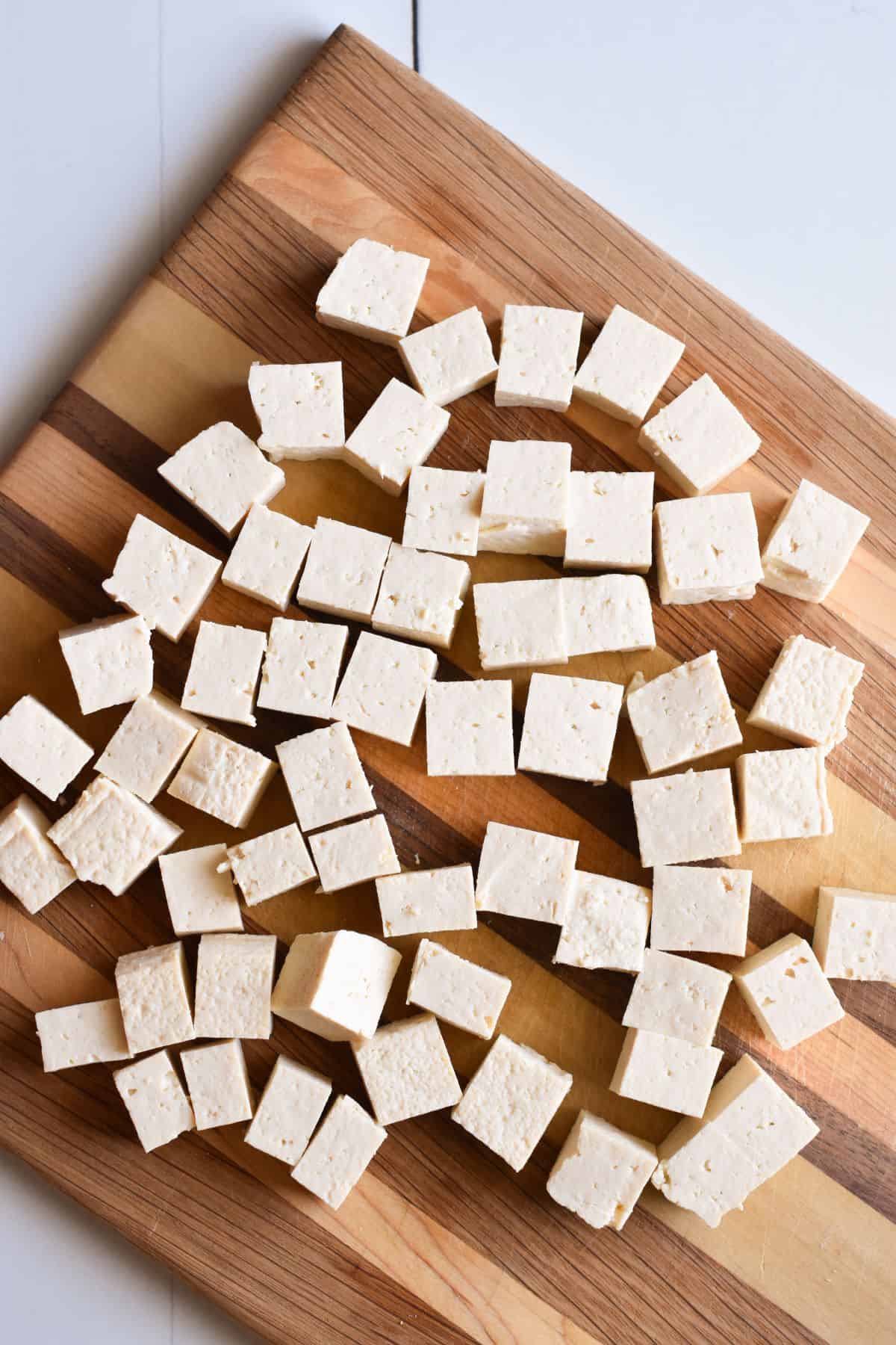 Tofu cut into cubes on a cutting board.