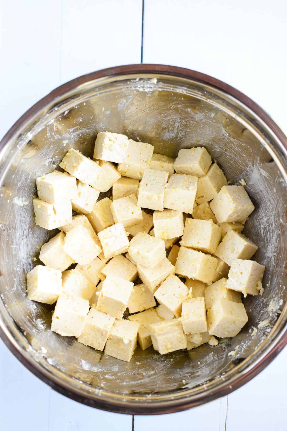 Tofu cut into cubes with coating in a mixing bowl.