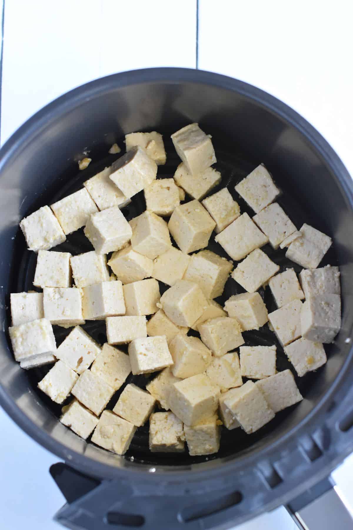 Cubes of tofu in air fryer basket.