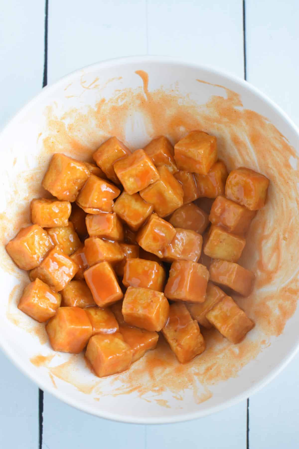 Cooked tofu cubes with buffalo sauce in a bowl.
