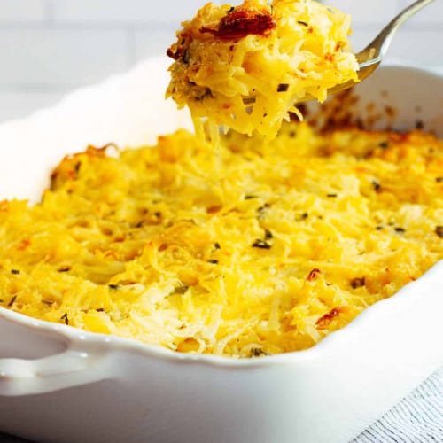 scooping out cheesy potatoes from a casserole dish.