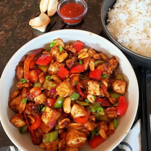 Bowl of kung pao tofu and rice with fortune cookies on the side.