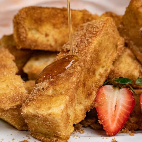 pouring syrup onto French toast sticks.