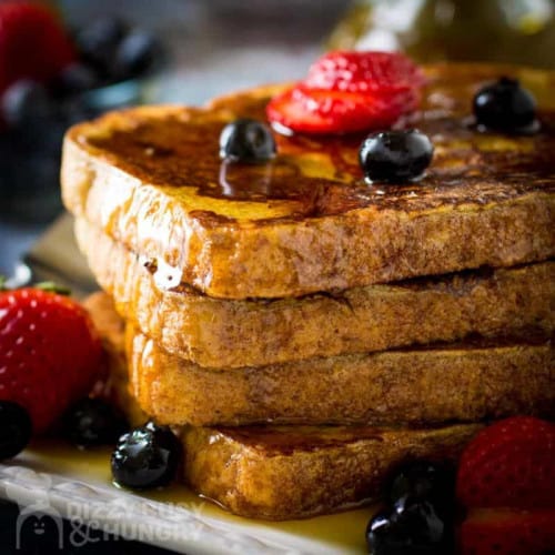 stack of cinnamon French toast on a plate with berries and syrup.